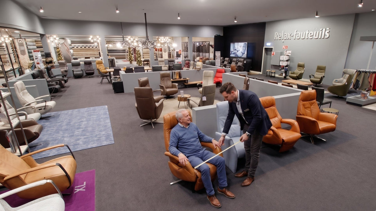 Adviseur helpt een klant bij het passen van een relaxfauteuil in de showroom van Hofmans at Home