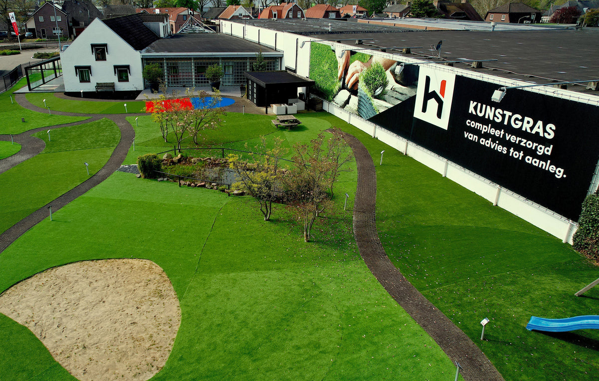 Kunstgras showtuin van Hofmans at Home van bovenaf, met paden, zandbak en speeltoestel