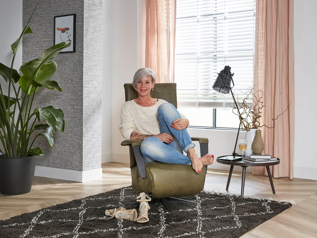 Vrouw zit ontspannen in een groene relaxfauteuil Brisa op een zwart-wit vloerkleed