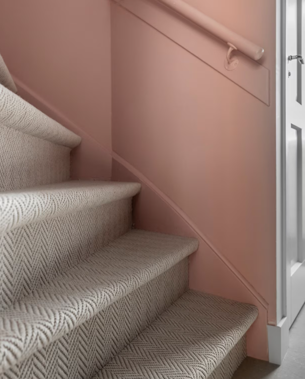 Trap met grijs-wit visgraat tapijt als trapbekleding langs een roze wand