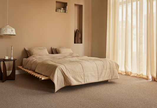 Slaapkamer met beige tapijt, laag houten bed en lichte vitrage voor het raam