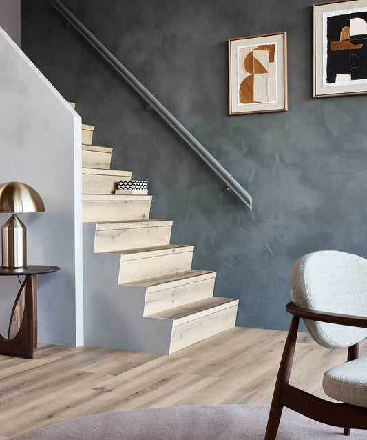 Gerenoveerde trap met lichte eikenhouten treden tegen een grijze wand, met fauteuil