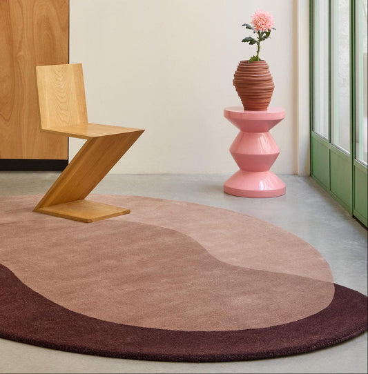 Vloerkleed op maat in vrije vorm met roze en bordeauxrode vlakken naast een houten stoel