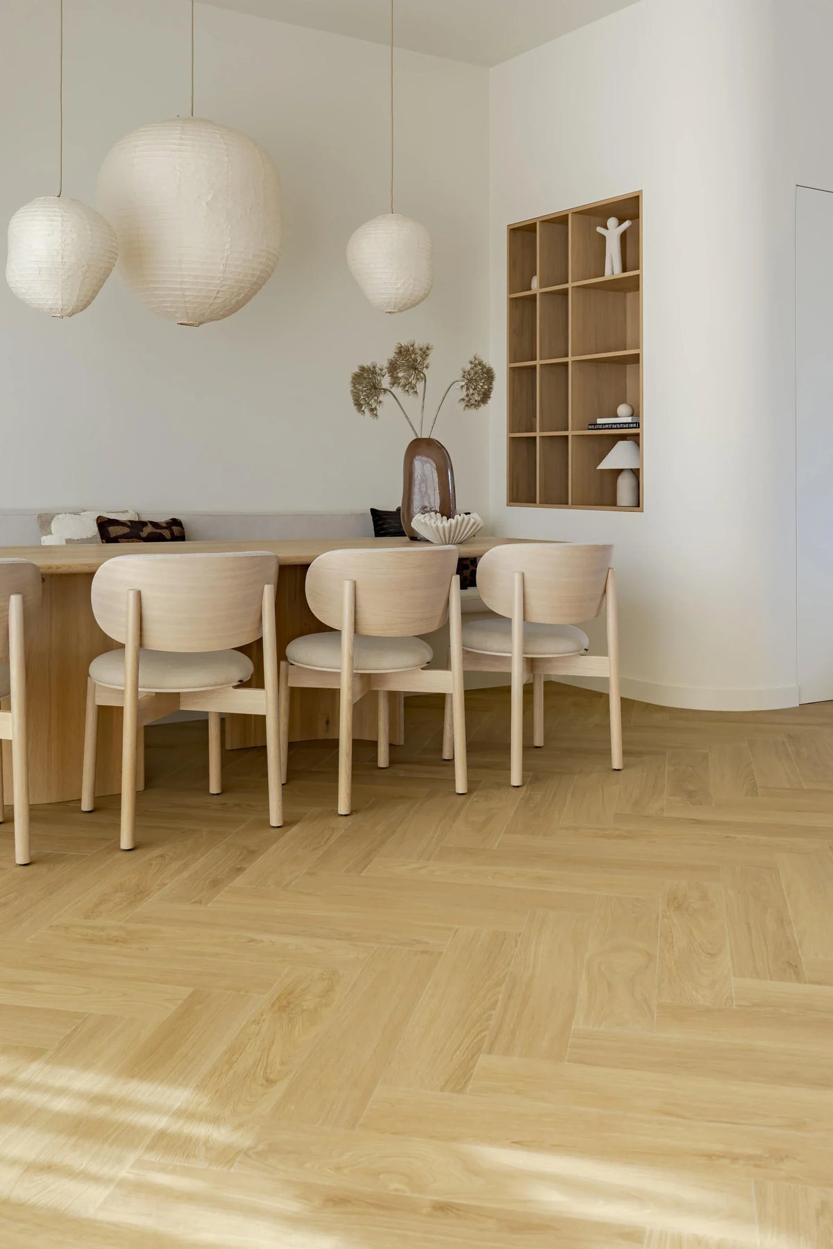 Eetkamer met lichte visgraatvloer, houten stoelen en witte plinten langs de wand