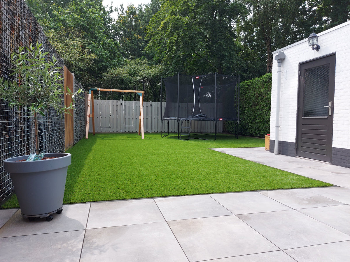 Tuin met kunstgras, schommel en trampoline voor kinderen naast een terras