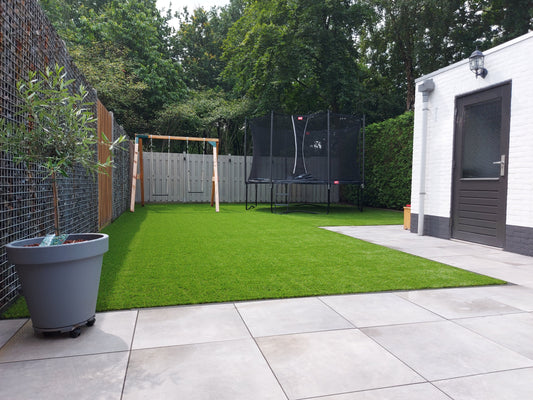 Tuin met kunstgras, schommel en trampoline voor kinderen naast een terras