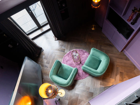 Boutique-hotelkamer met visgraatvloer, groene fauteuils en roze vloerkleed, van bovenaf