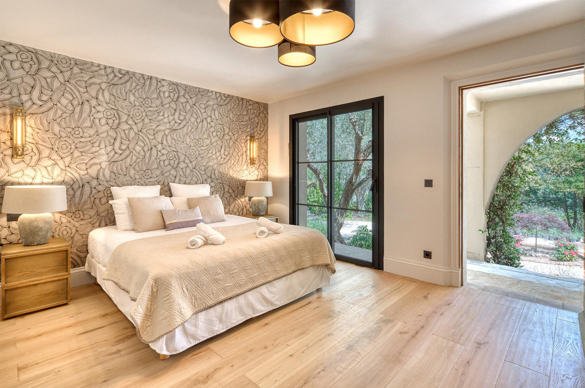 Slaapkamer met grafisch behang achter het bed, lichte houten vloer en openslaande deuren