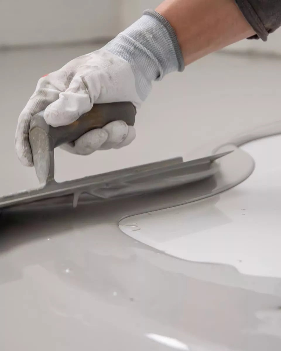 Close-up van een hand met handschoen die een gietvloer gladstrijkt met een spaan