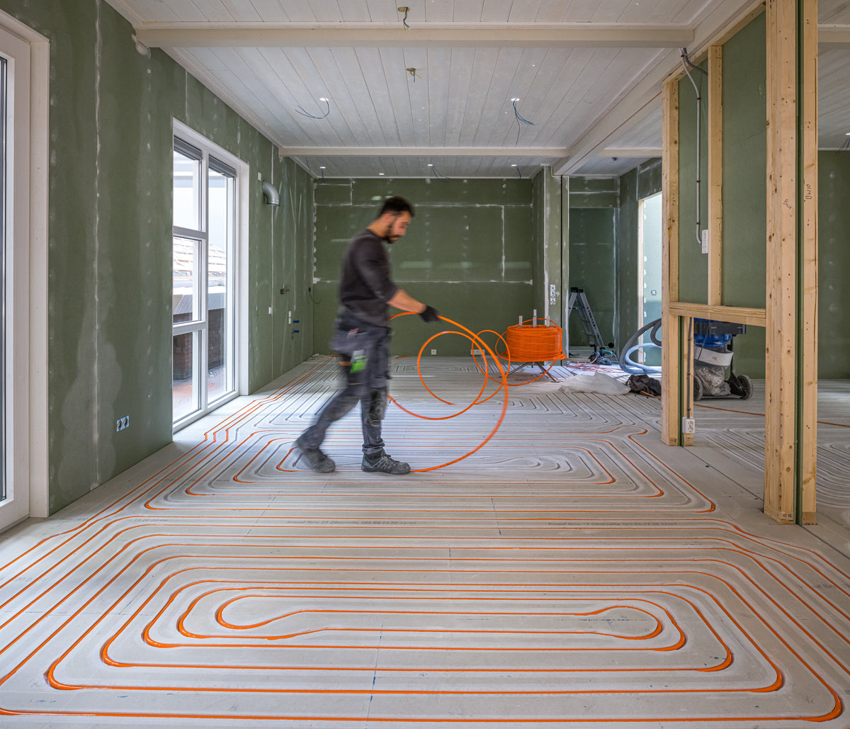 Installateur legt vloerverwarmingsbuizen in een slingerpatroon op een ondervloer tijdens een verbouwing