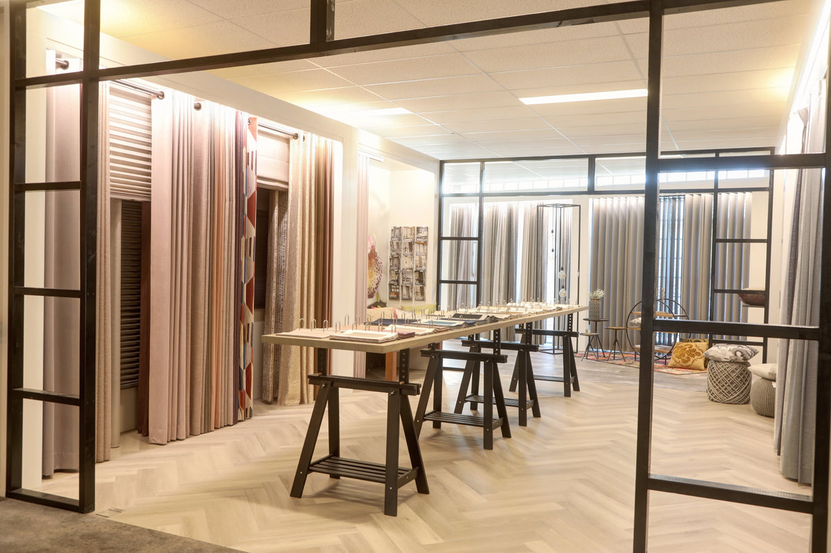 Gordijnenafdeling in de showroom van Hofmans at Home met stoffen en een stalentafel
