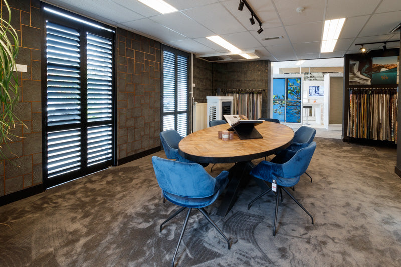 Adviesruimte met zwarte shutters, ovale houten tafel en blauwe stoelen in de showroom