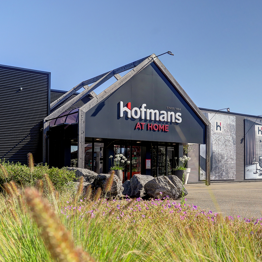 Entree van Hofmans at Home in Cuijk met logo op de gevel en bloeiende siergrassen