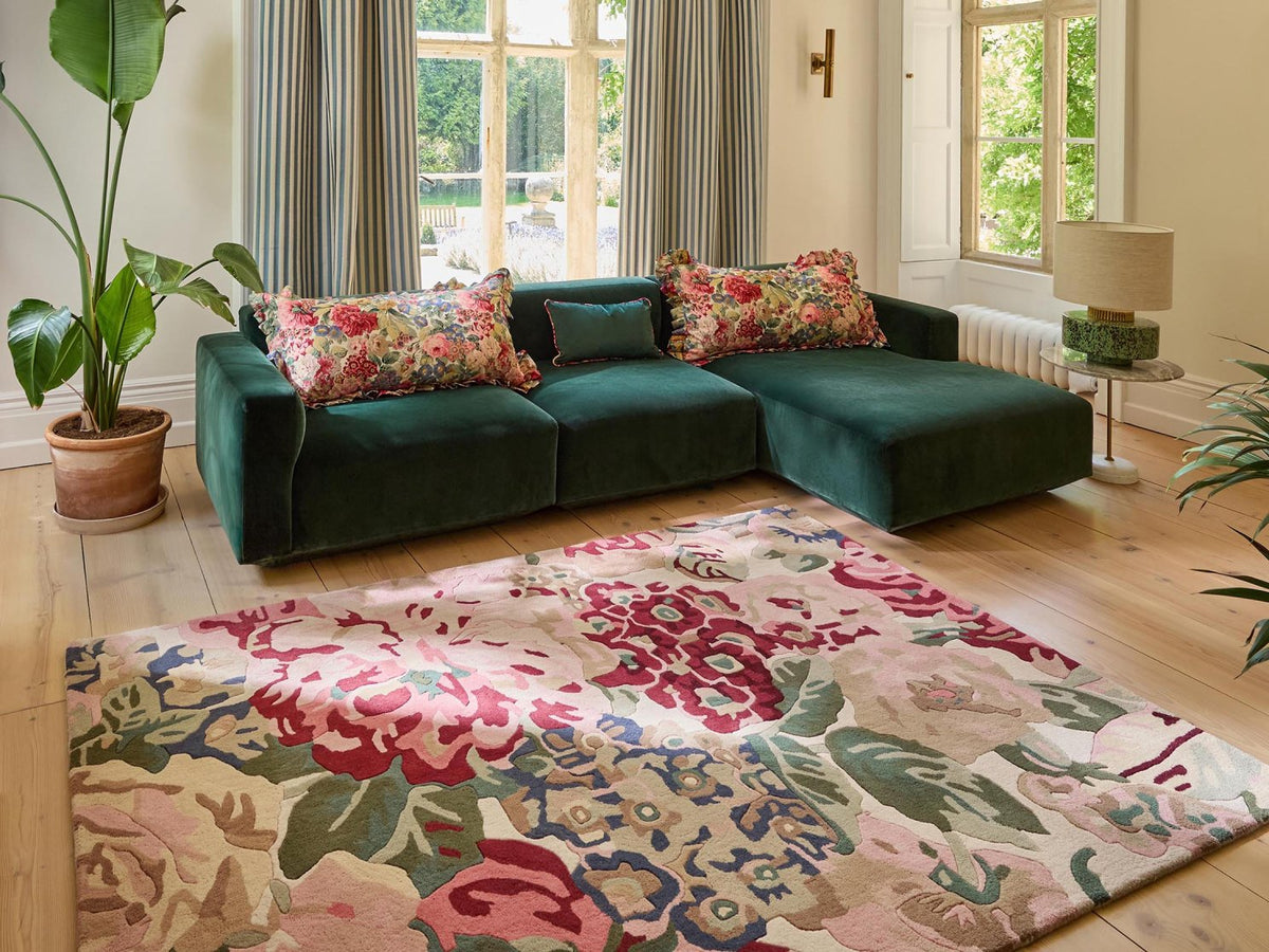 Woonkamer met groene fluwelen hoekbank en een kleurrijk vloerkleed met rozen en pioenen