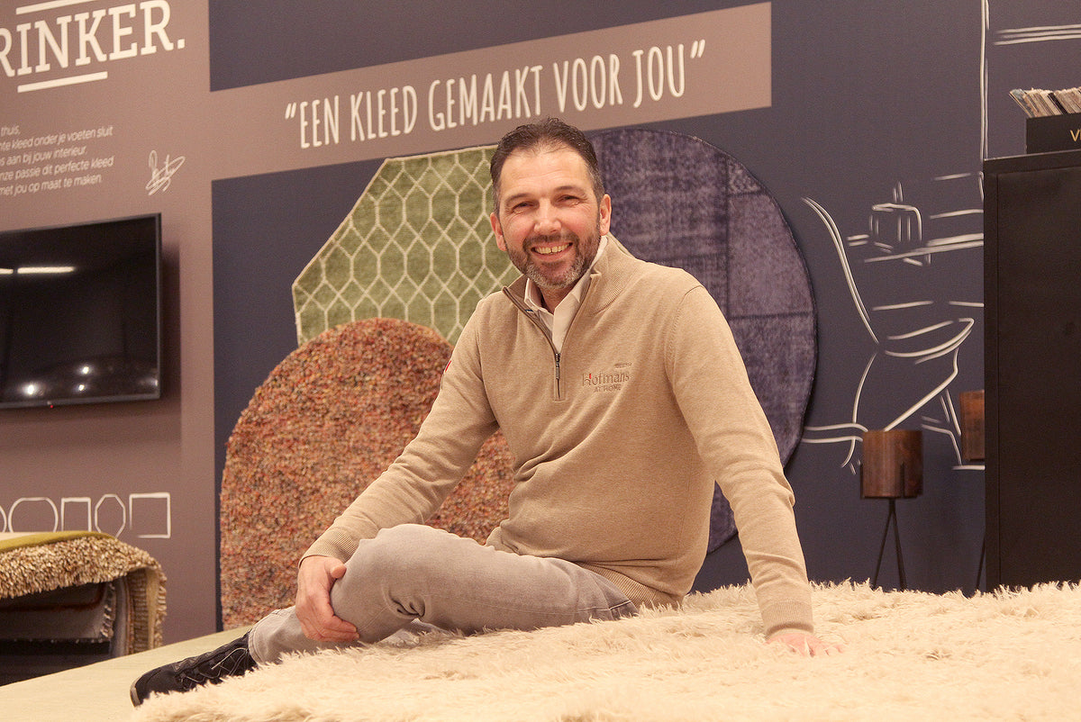 Adviseur Erik zit op een hoogpolig vloerkleed bij de vloerkledenwand in de showroom van Hofmans at Home
