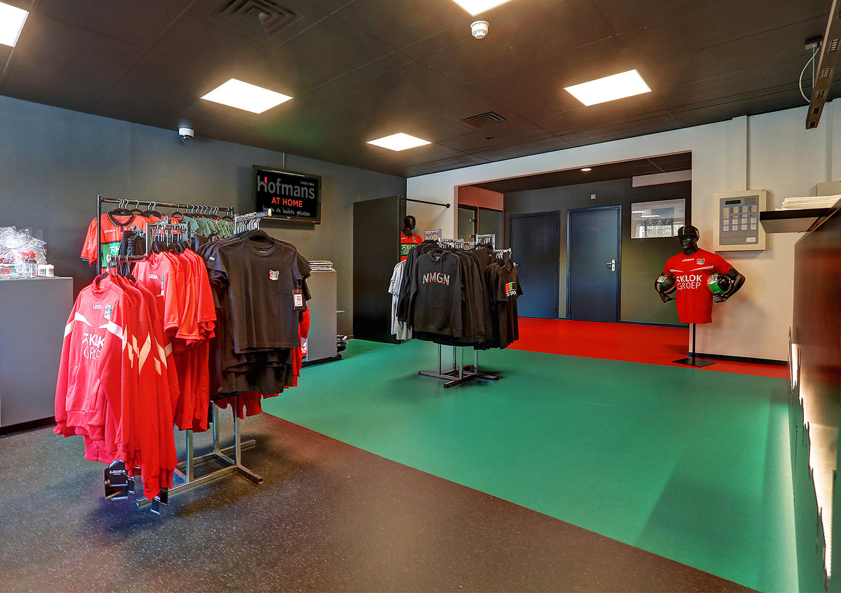 Fanshop van NEC Nijmegen met groene vloer, kledingrekken met rode en zwarte shirts