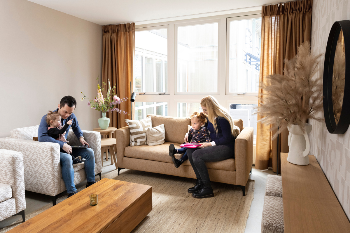 Gezin met kinderen in een woonkamer met bruine gordijnen, banken en houten salontafel