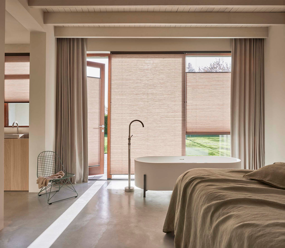 Lichte slaapkamer met plissé raamdecoratie, linnen gordijnen, betonlook vloer en vrijstaand bad