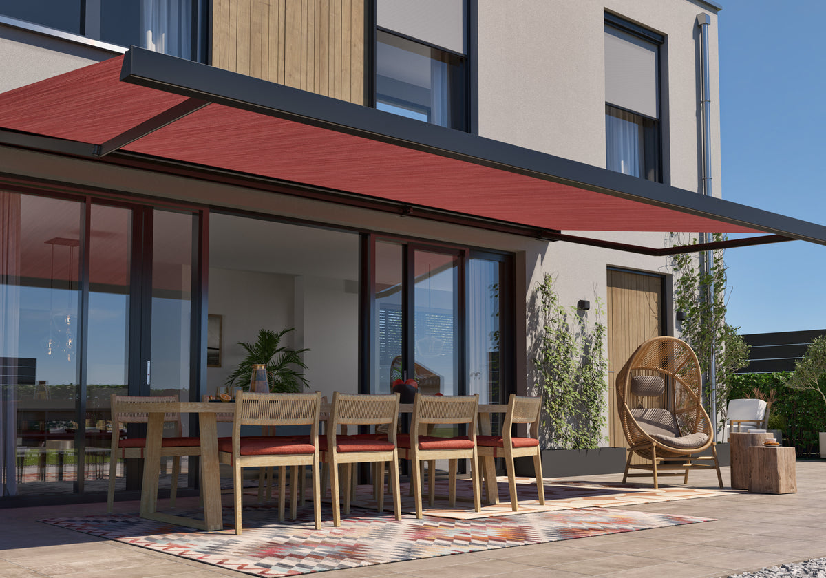 Terras met rood knikarmscherm boven een buitentafel met stoelen en een vloerkleed