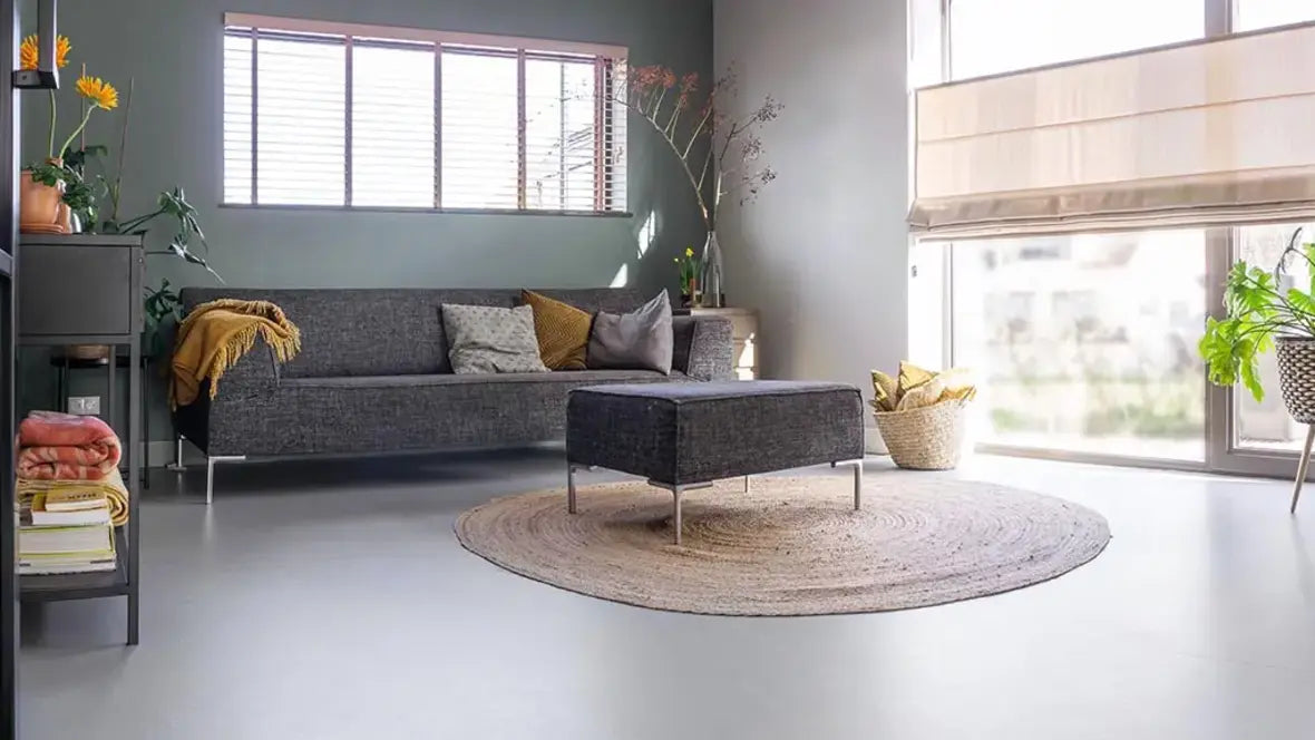 Woonkamer met lichtgrijze Forbo Marmoleum vloer, grijze hoekbank, rond jute vloerkleed en raamdecoratie