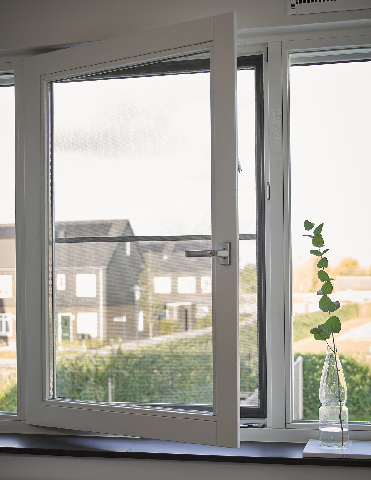 Openstaand wit raam met uitzicht op nieuwbouwwoningen en een vaas met eucalyptus