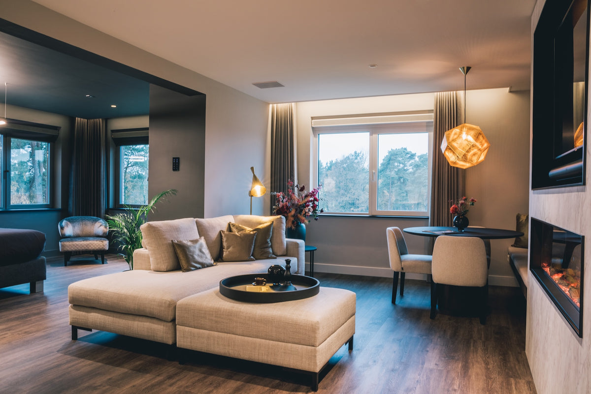 Hotelsuite met donkere houten vloer, beige loungebank, eethoek en sfeerhaard