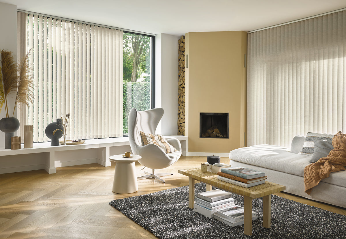 Woonkamer met crèmekleurige verticale lamellen, visgraatvloer, open haard en witte fauteuil
