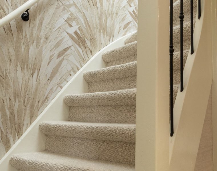 Trap met beige wollen tapijt als trapbekleding, zwarte spijlen en behang met bladmotief