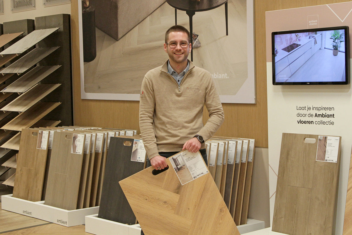 Adviseur Luuk met een laminaatstaal in visgraat bij de Ambiant collectie in de showroom