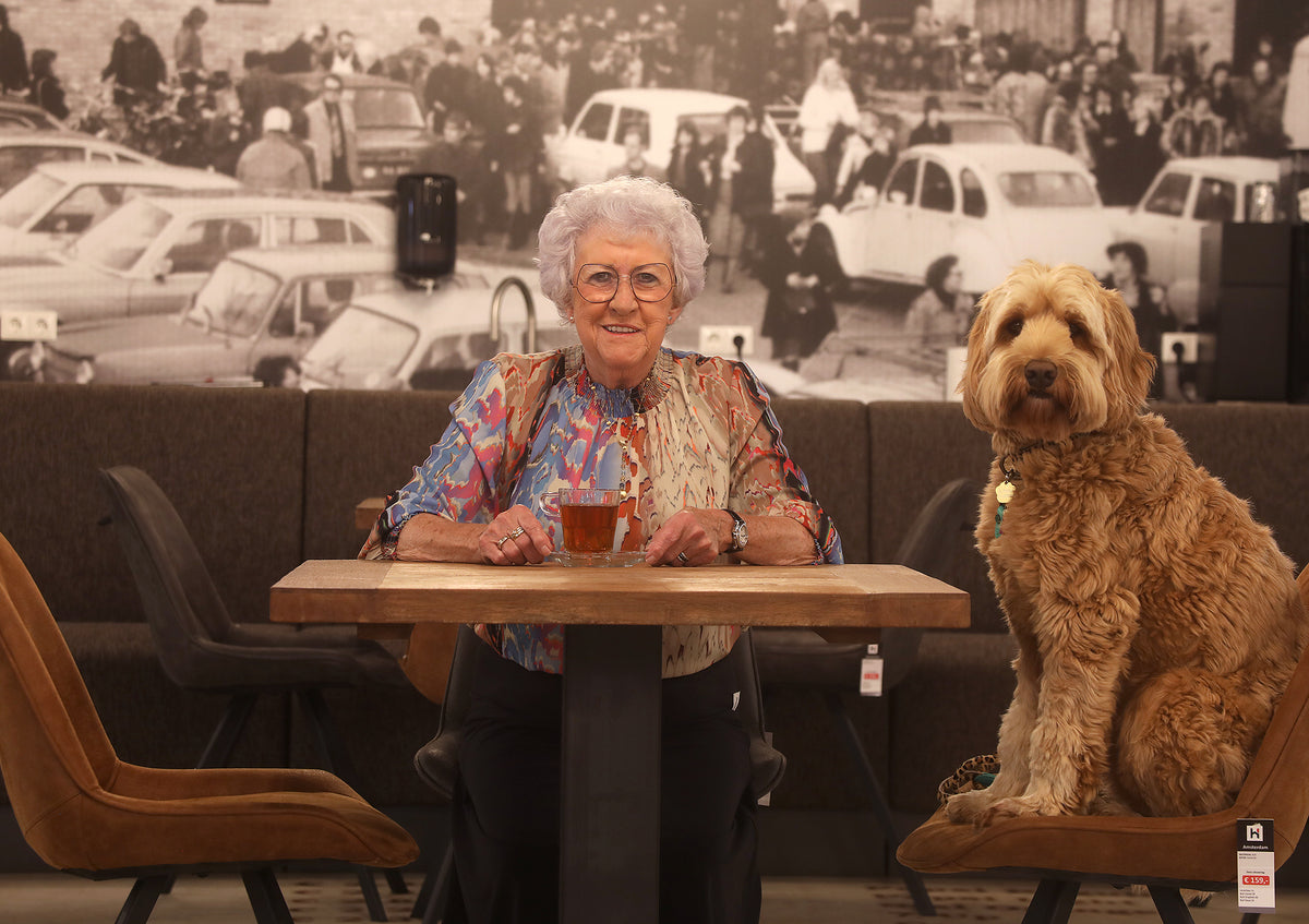 Mientje Hofmans en hond Jaap aan een tafel voor een historische zwart-witfoto bij Hofmans at Home