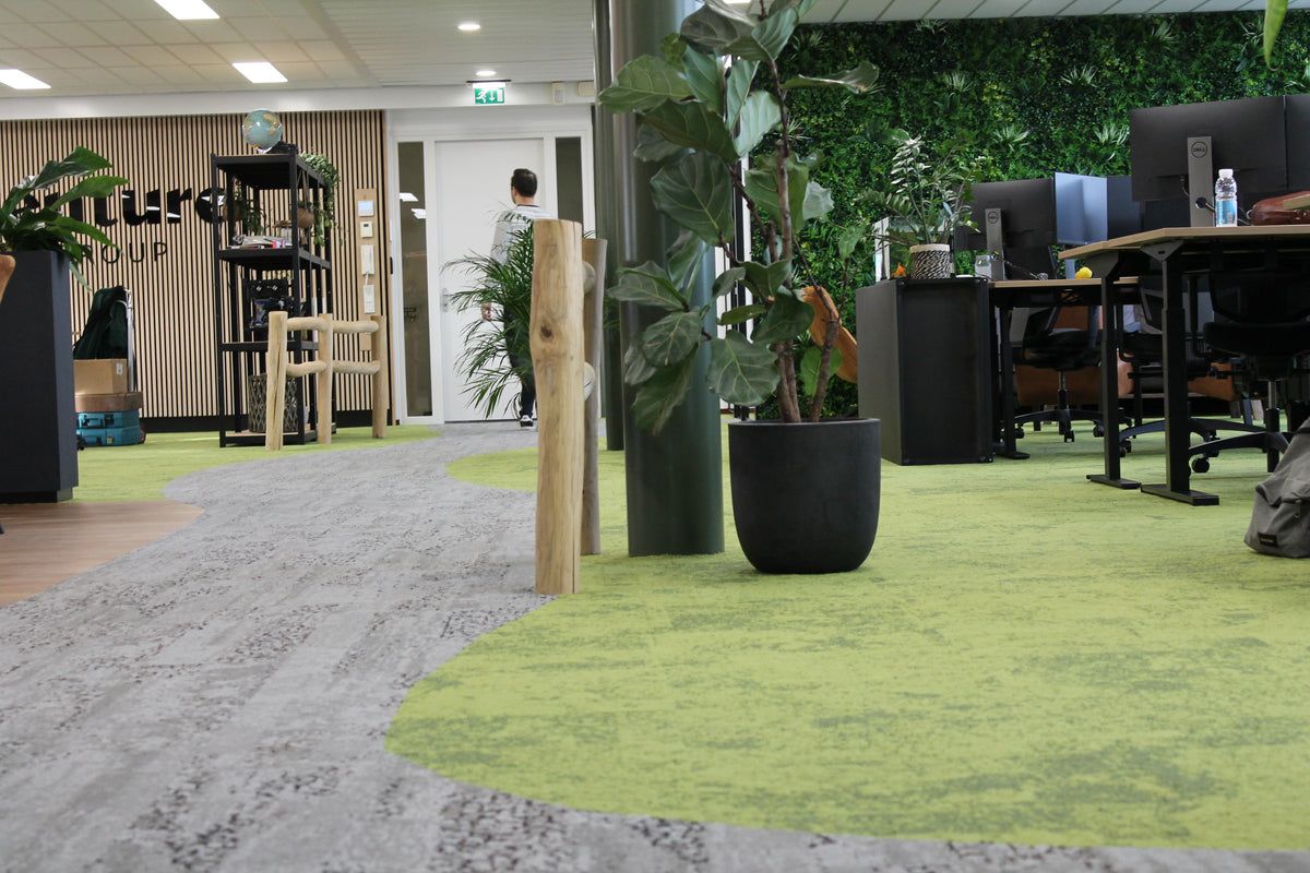 Kantoortuin met grijze en groene tapijttegels, bureaus, planten en groene wand