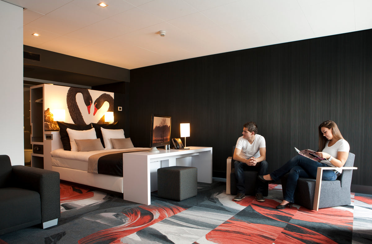 Hotelkamer met kleurrijk vloerkleed in rood en grijs, tweepersoonsbed, bureau en zithoek
