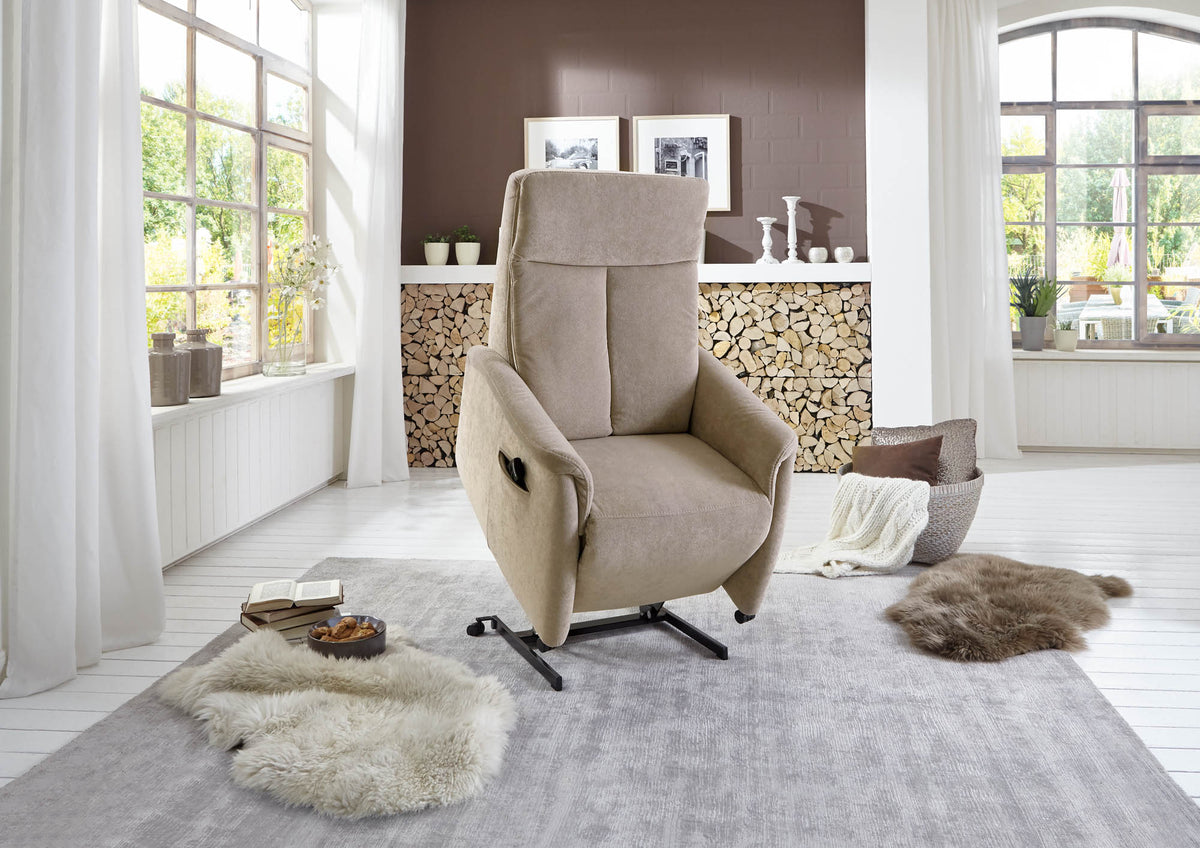 Beige sta-op relaxfauteuil op grijs vloerkleed in een lichte woonkamer met haardhout