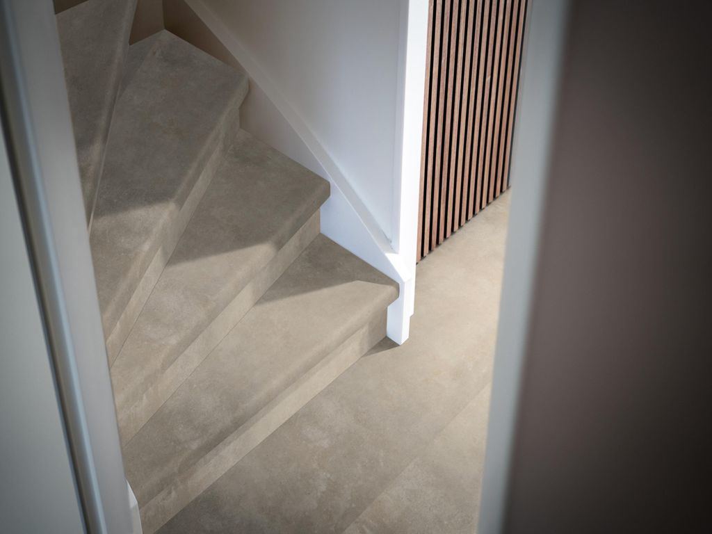 Trap en vloer in hetzelfde grijze steenlook PVC, met witte trapleuning en houten lattenwand
