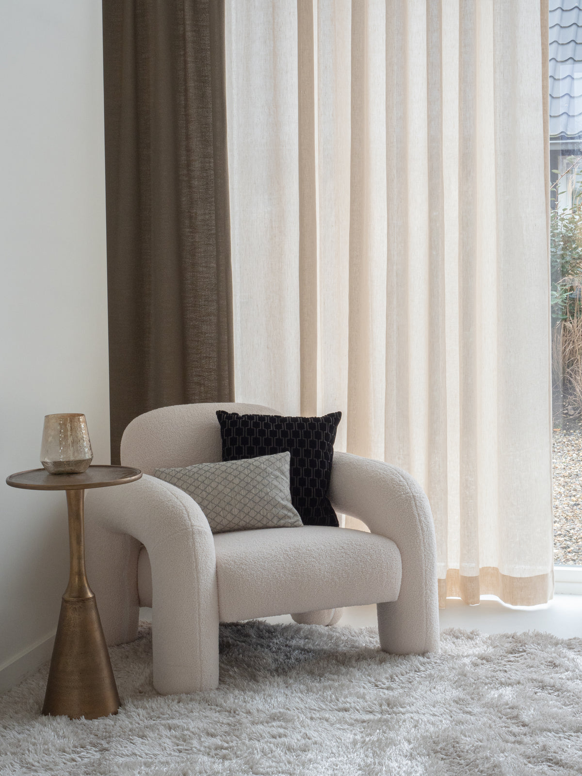 Bouclé fauteuil voor lichte linnen gordijnen en taupe overgordijn op hoogpolig vloerkleed