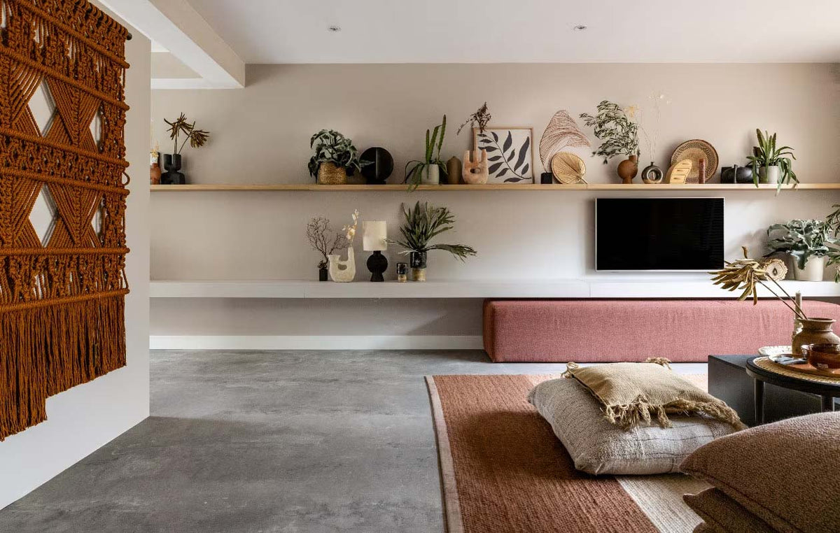 Woonkamer met grijze vinylvloer in betonlook, roze bank en wandplanken met decoratie