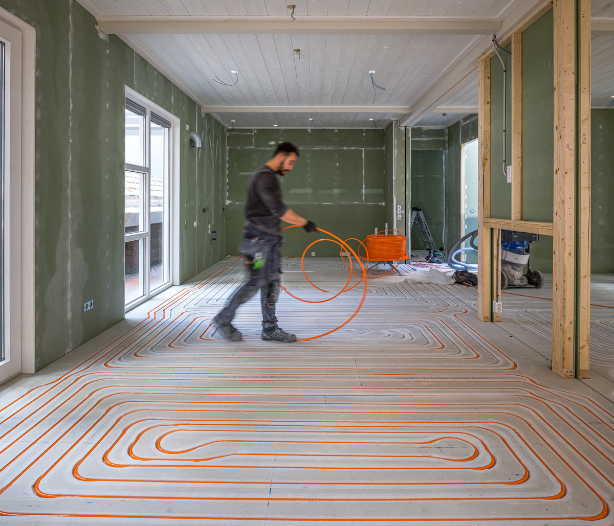 Installateur legt vloerverwarmingsbuizen in een slingerpatroon op een ondervloer tijdens een verbouwing