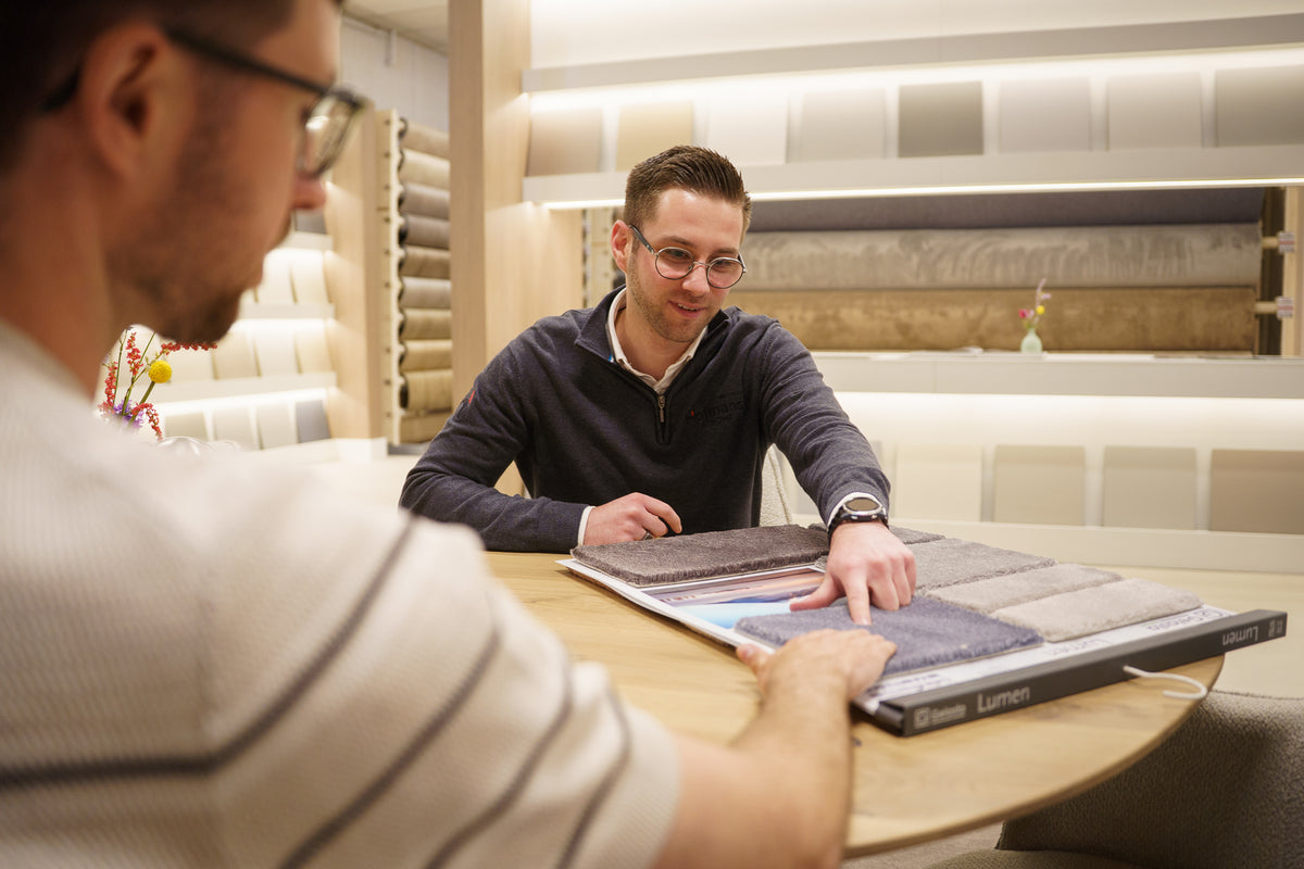 Adviseur Luuk bespreekt tapijt- en vloerstalen met een klant in de showroom van Hofmans at Home
