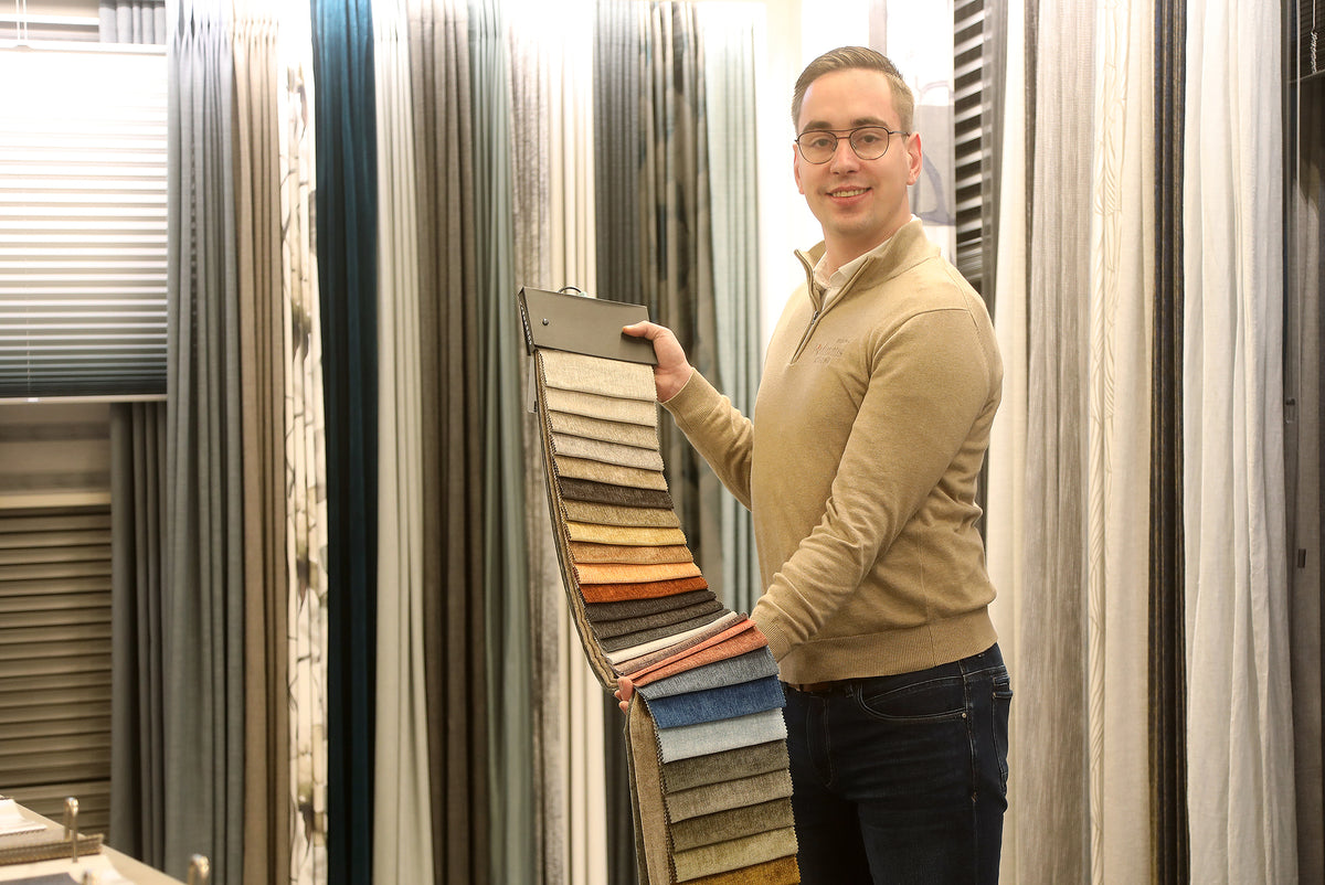 Adviseur Robert van Hofmans at Home toont een groot stoffenstalenboek met verschillende gordijnstoffen in de showroom voor persoonlijk raamdecoratieadvies.