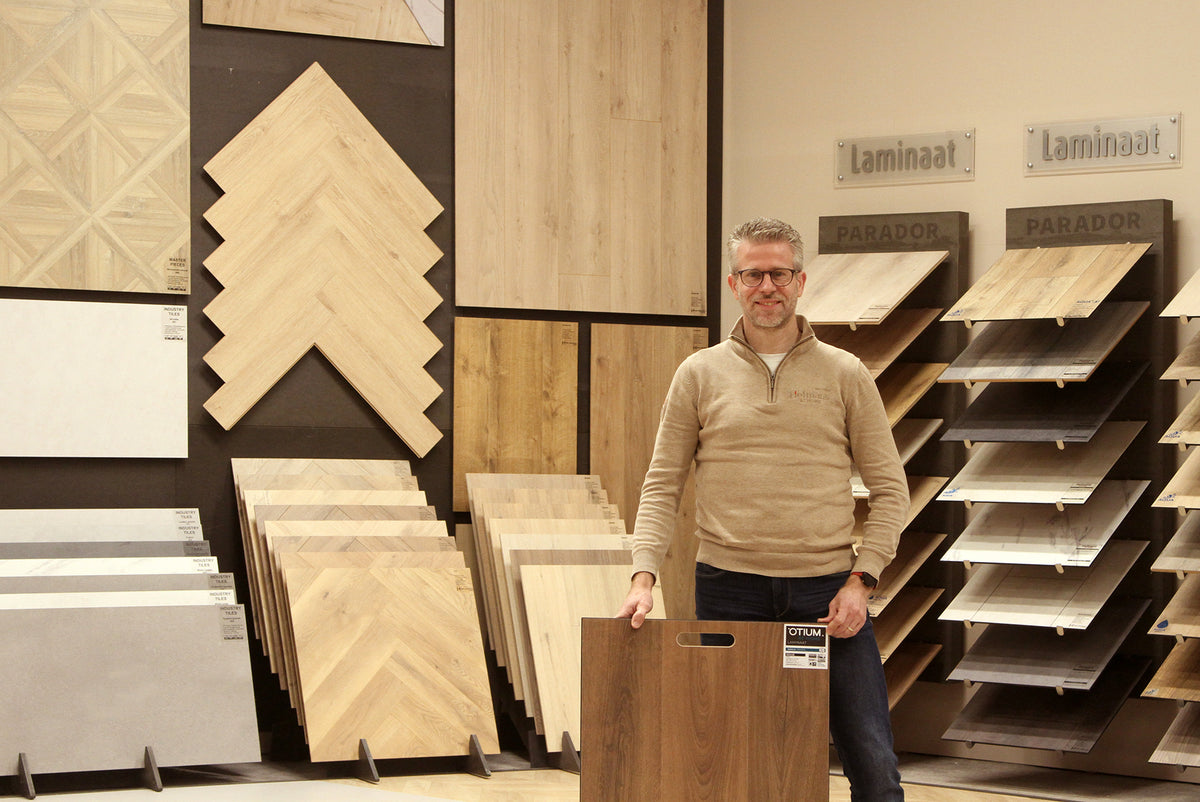 Showroom van Hofmans at Home met laminaatvloeren, waar productspecialist Michel een vloerstaal vasthoudt tussen verschillende vloeropstellingen