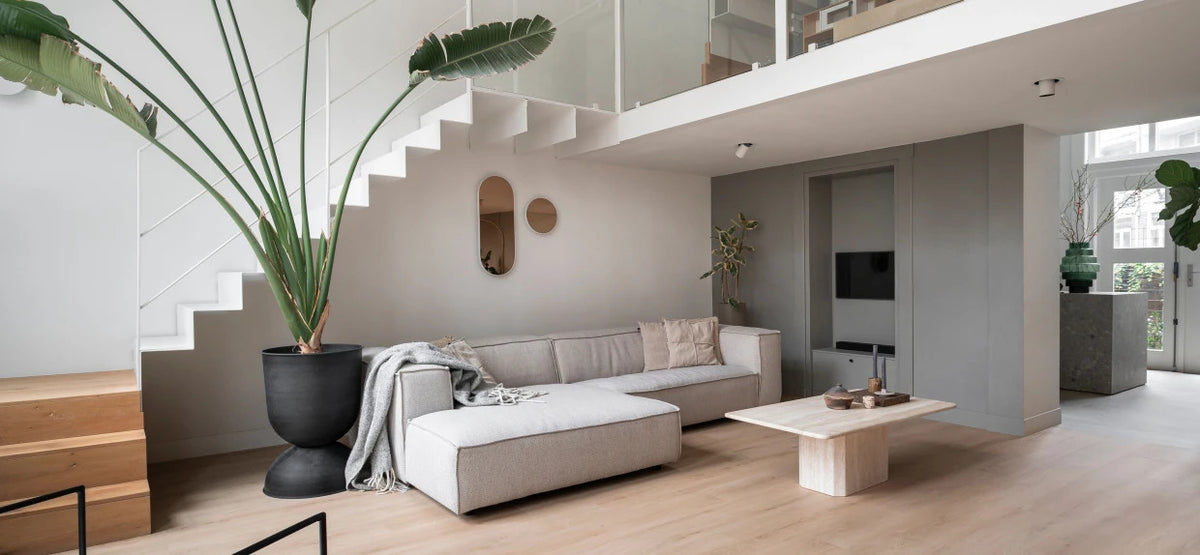 Moderne lichte woonkamer met grote hoekbank, houten vloer, strakke trap en minimalistische inrichting.