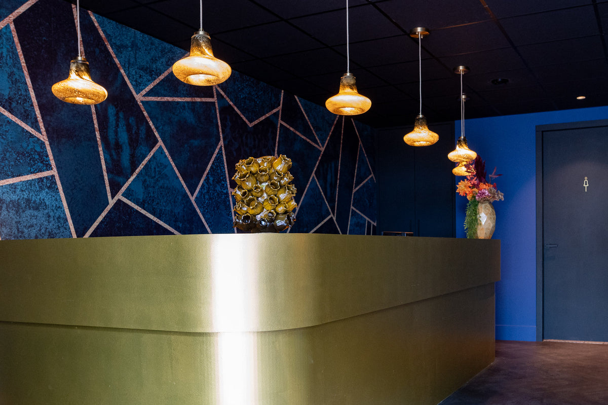 Receptie van Hotel De Bungelaer met goudkleurige balie, blauwe wand en glazen hanglampen