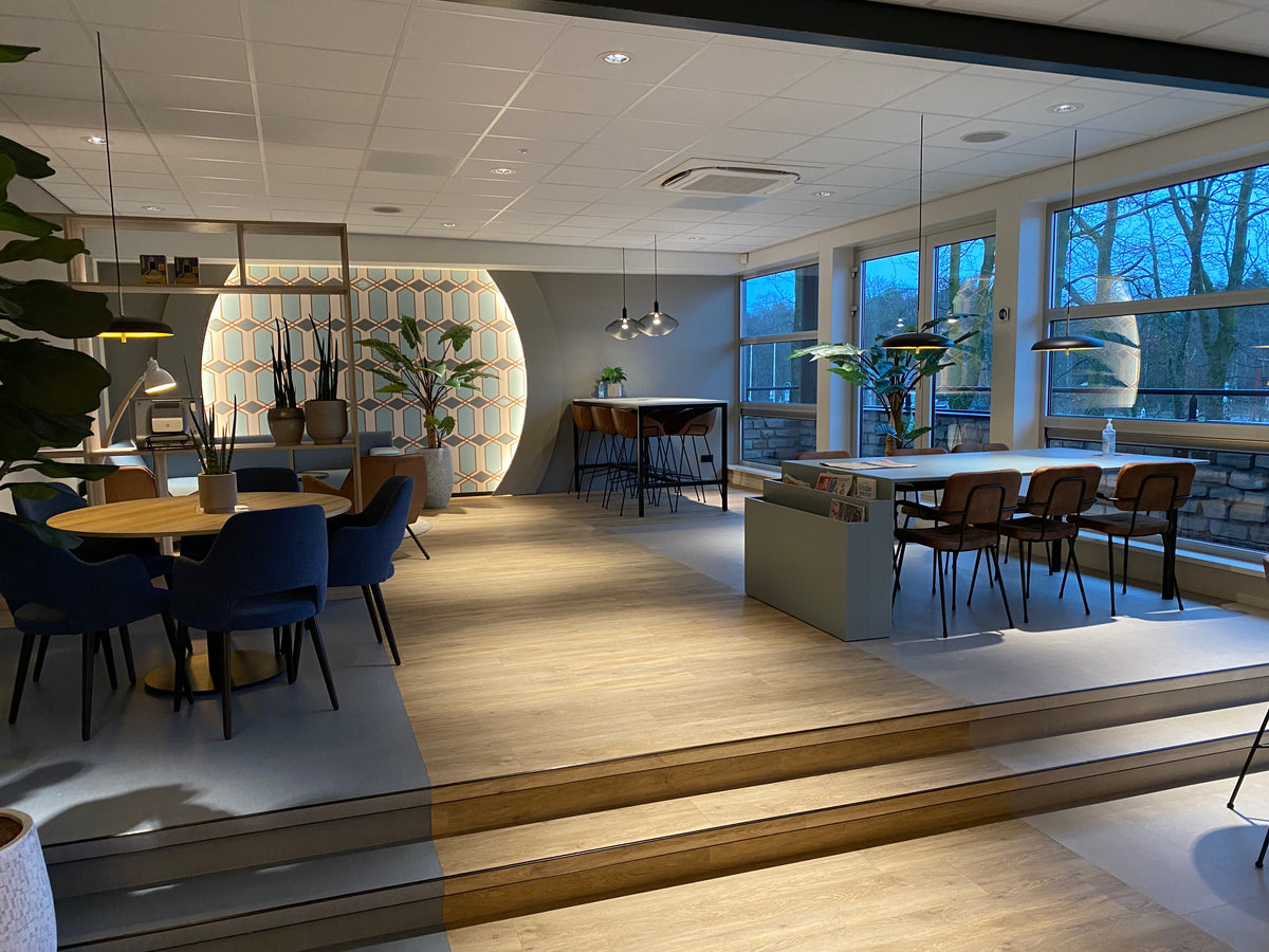 Kantoorruimte met verhoogde houten vloer, tafels, blauwe stoelen en grote ramen
