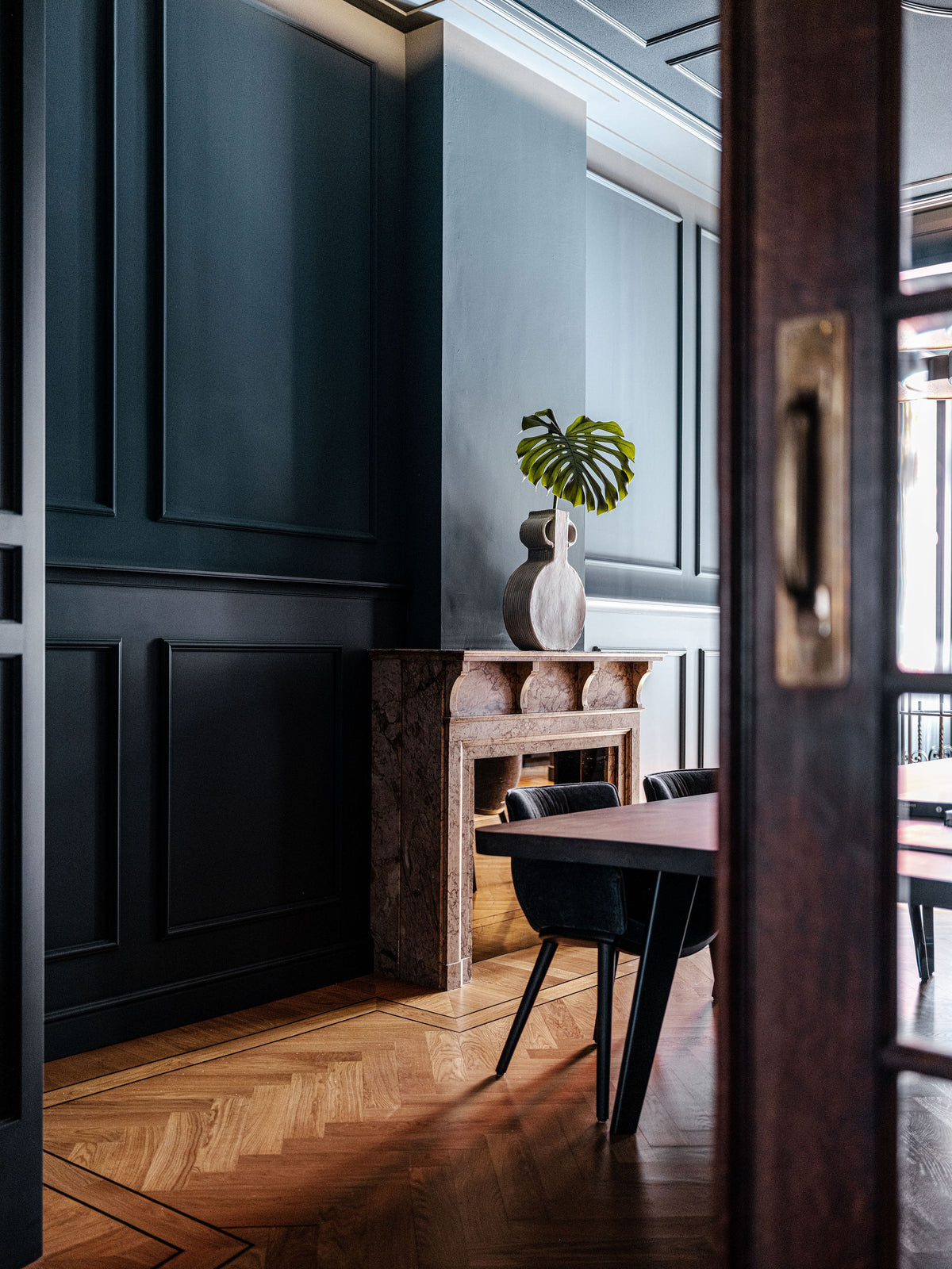Kamer met donkerblauwe wandpanelen, visgraat parketvloer en marmeren schouw