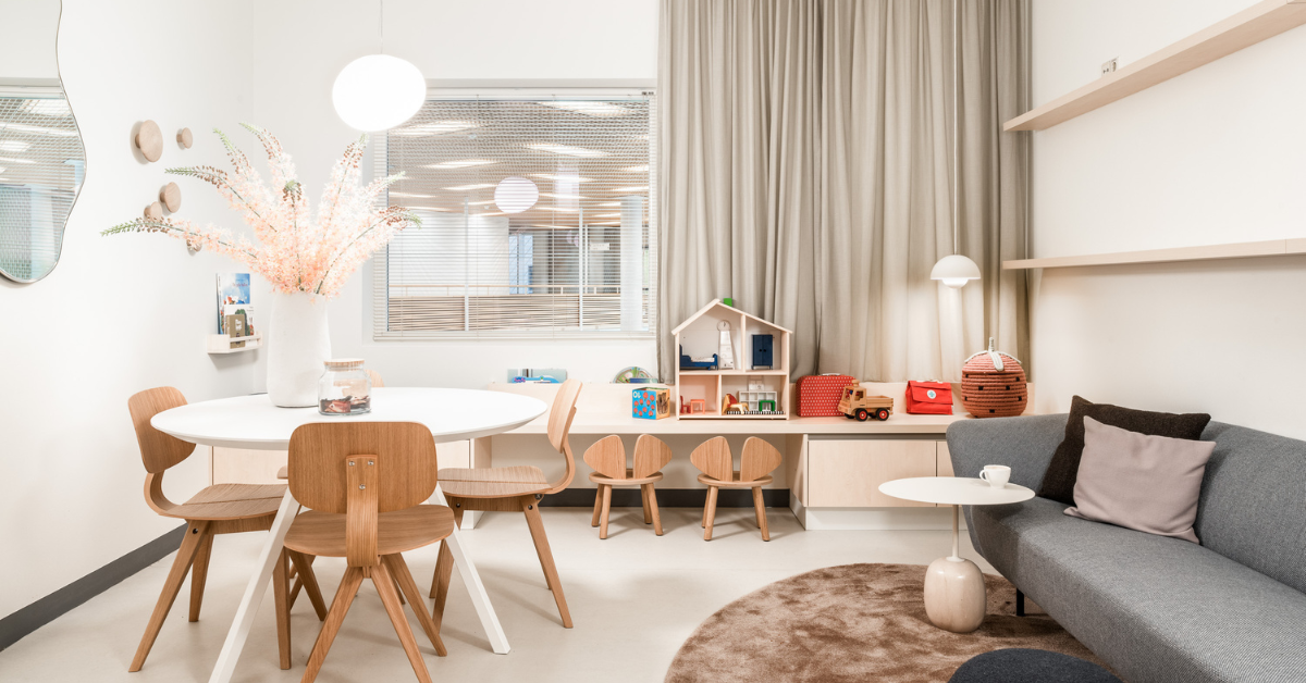 Kindvriendelijke wachtruimte met lichte vloer, ronde tafel, bank en speelhoek