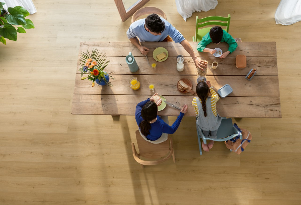 Gezin aan een houten tafel op een Quick-Step PVC-vloer in licht eikendecor, van bovenaf