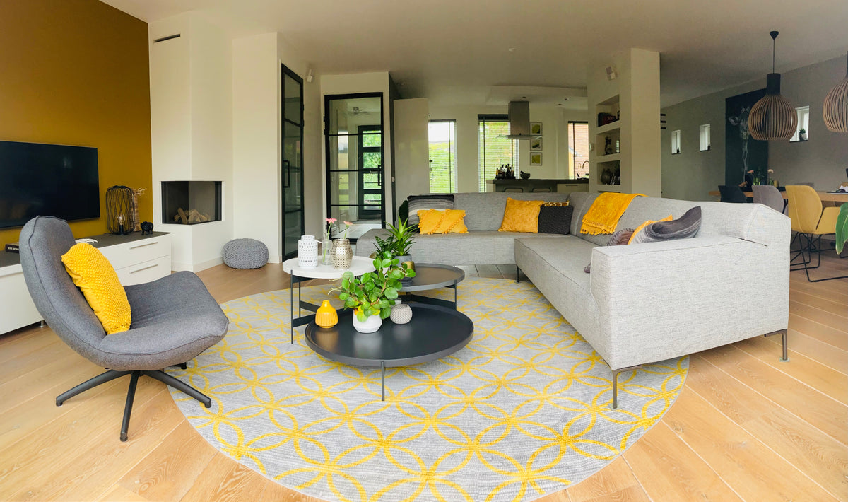 Recent opgeleverde woonkamer met lichte houten vloer, grijze hoekbank en rond geel vloerkleed