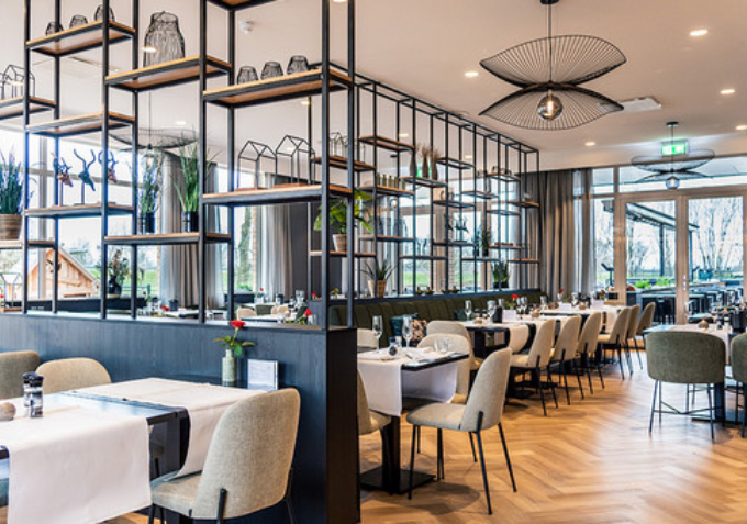Modern restaurantinterieur bij Van der Valk Cuijk met open rekkenwand, stijlvolle beige stoelen, gedekte tafels, houten visgraatvloer, grote ramen en warme eigentijdse sfeer.