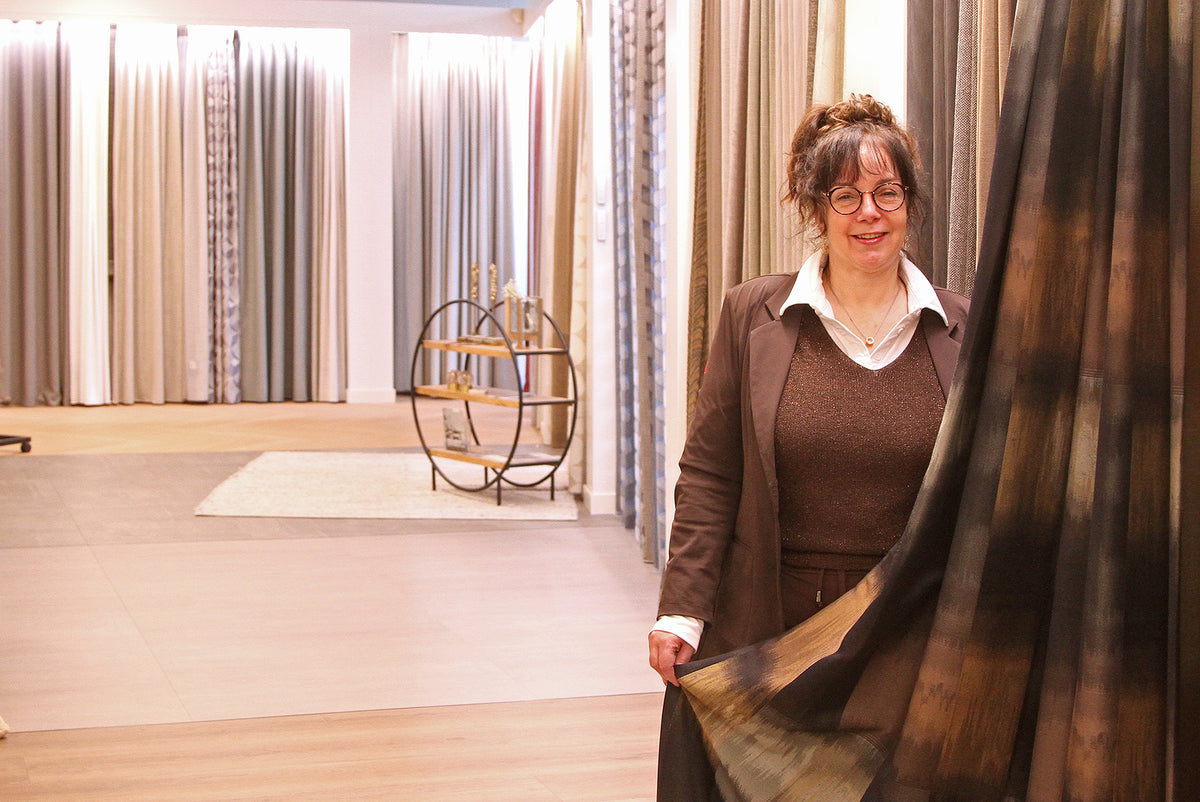 Showroombeeld van Hofmans at Home met verschillende soorten raamdecoratie, waarbij productspecialist Natasja een gordijnstof toont