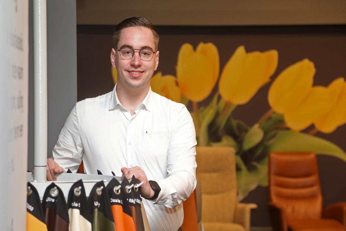 Adviseur Robert in de relaxfauteuil hoek van Hofmans at Home met een selectie lederstalen, voor een wand met gele tulpen en omringd door comfortabele fauteuils.